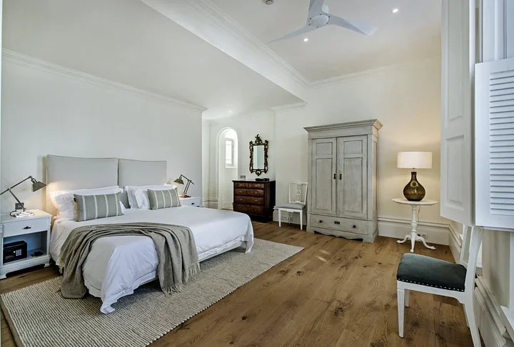 Spacious bedroom with a king bed, wood floors, a gray painted armoire, and an antique chest of drawers