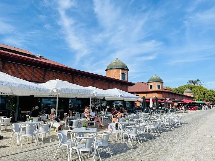 Red brick market halls with green domed towers and caf&eacute; tables with white umbrellas along the waterfront in Olh&atilde;o