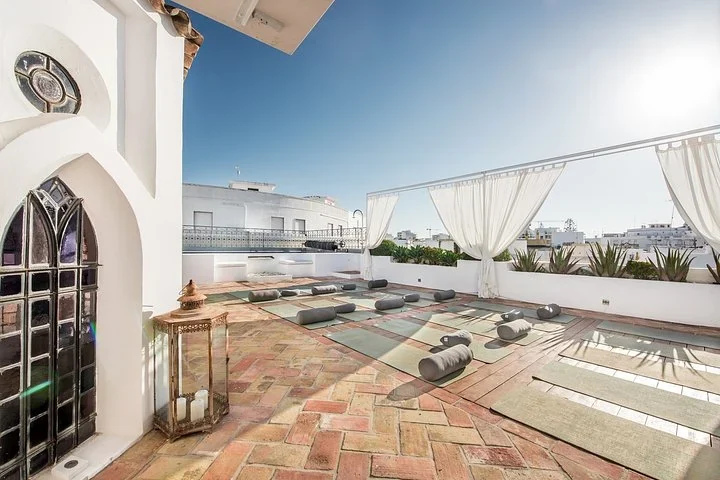 Algarve yoga retreat mats and bolsters set out on a sunny rooftop terrace beside a small white chapel in Olh&atilde;o