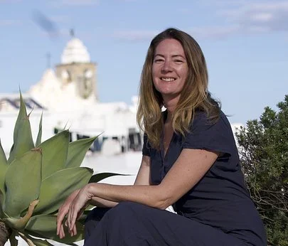 Amy Heinemann smiling beside an agave plant with a white church dome behind her