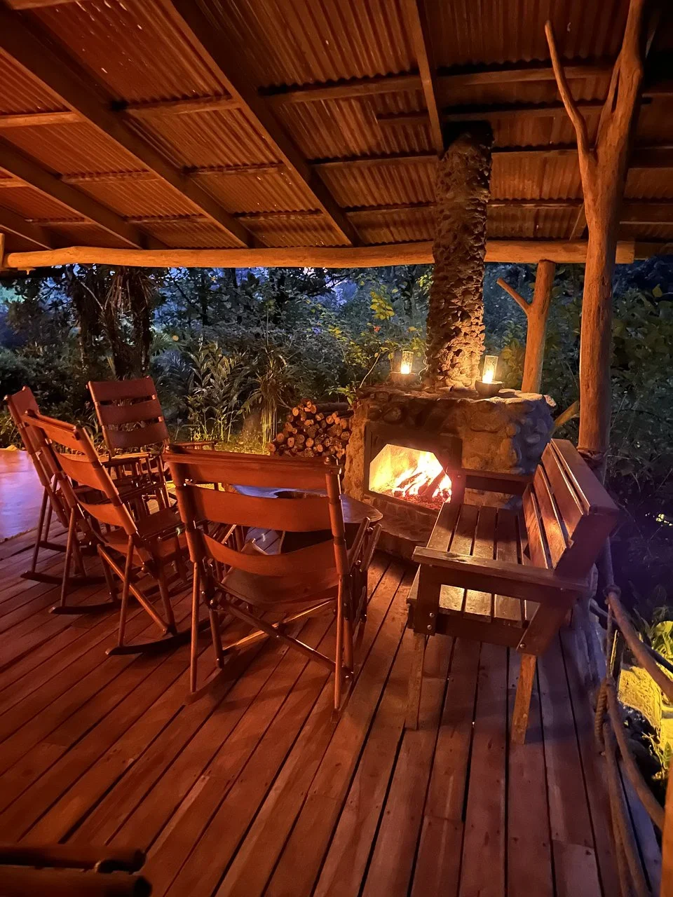 Fire burning in a stone fireplace on a covered wooden porch with rocking chairs at dusk