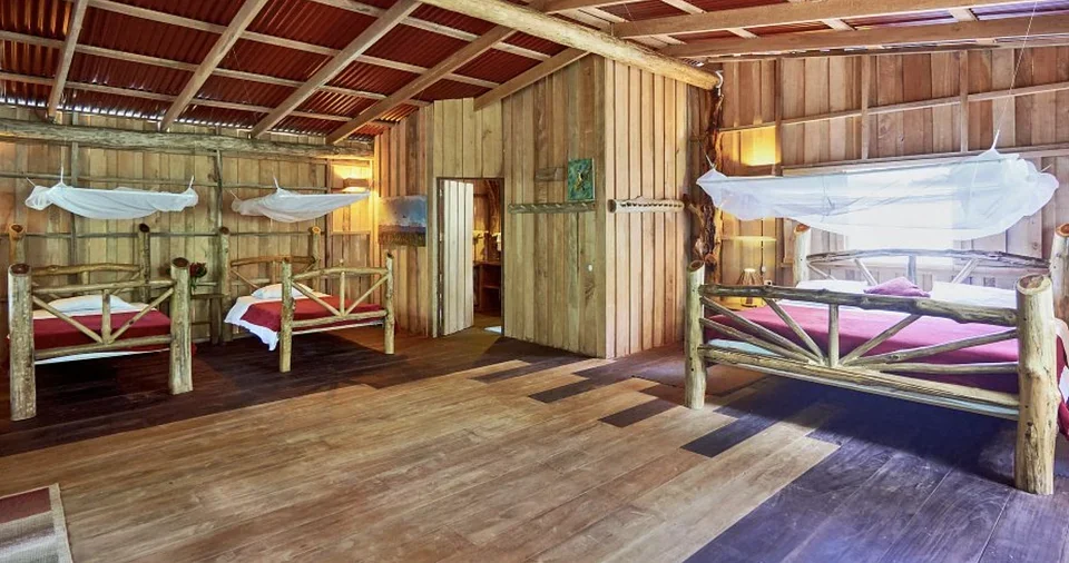 Spacious wood cabin interior with three log-framed beds and mosquito nets at the Costa Rica retreat lodge