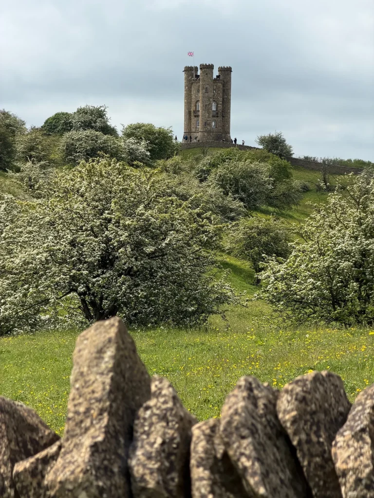 Broadway Tower on a hilltop above white hawthorn blossom and a dry stone wall