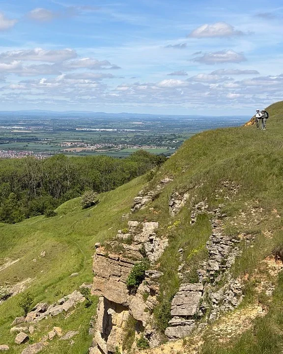 Walker standing on a grassy escarpment edge above a wide valley and distant hills
