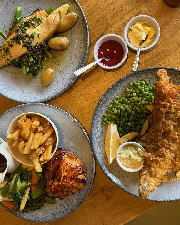 Pub lunch of fish and chips with peas, a golden pie with chips, and grilled fish on a wooden table