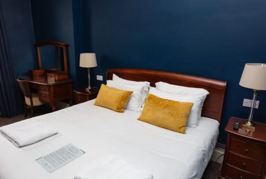Hotel room with a double bed, gold pillows, and navy walls