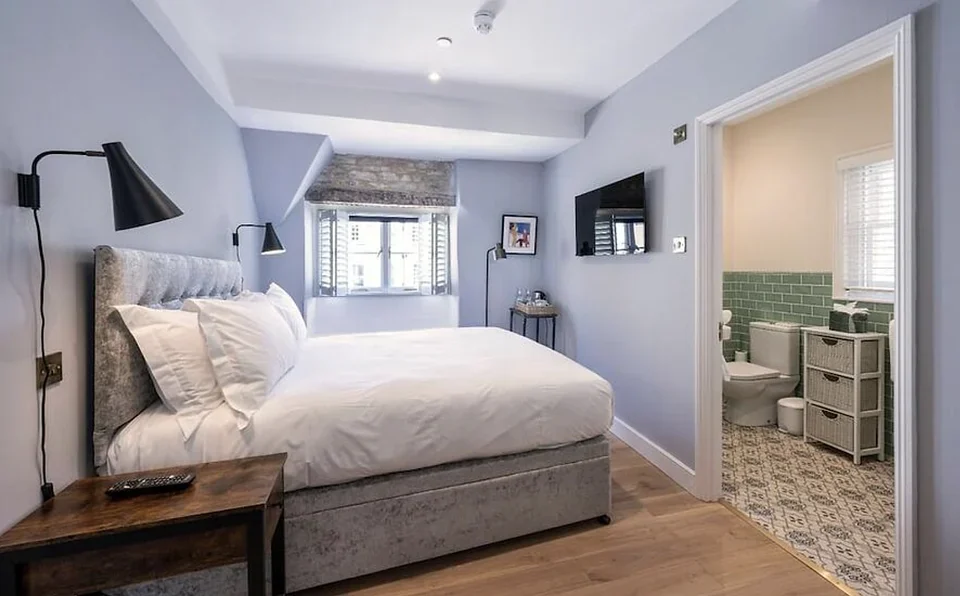 Bright hotel room with a large white bed, wall lamps, and an en-suite bathroom