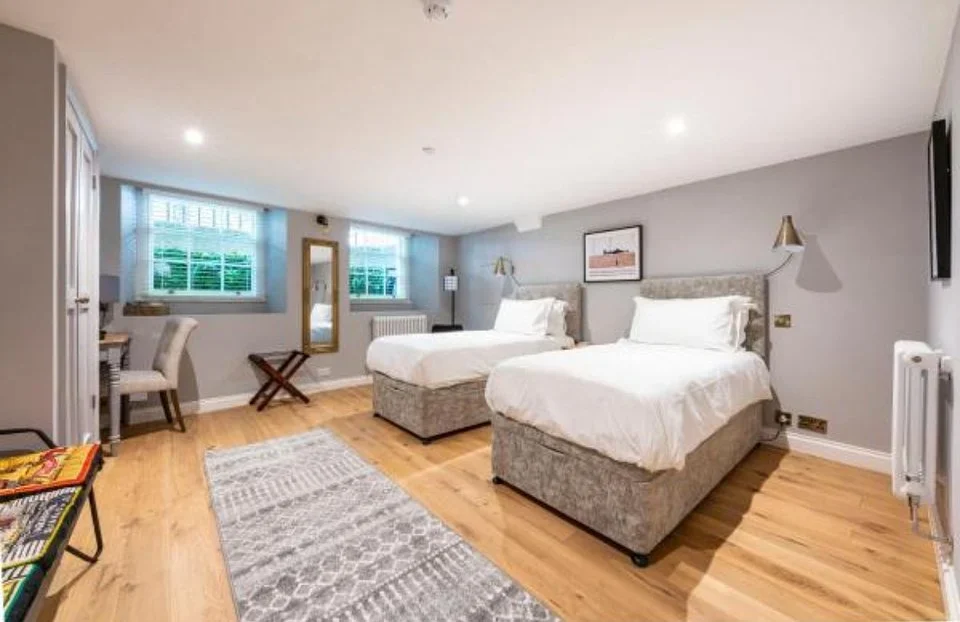 Bright hotel room with two twin beds, wood floors, and a writing desk