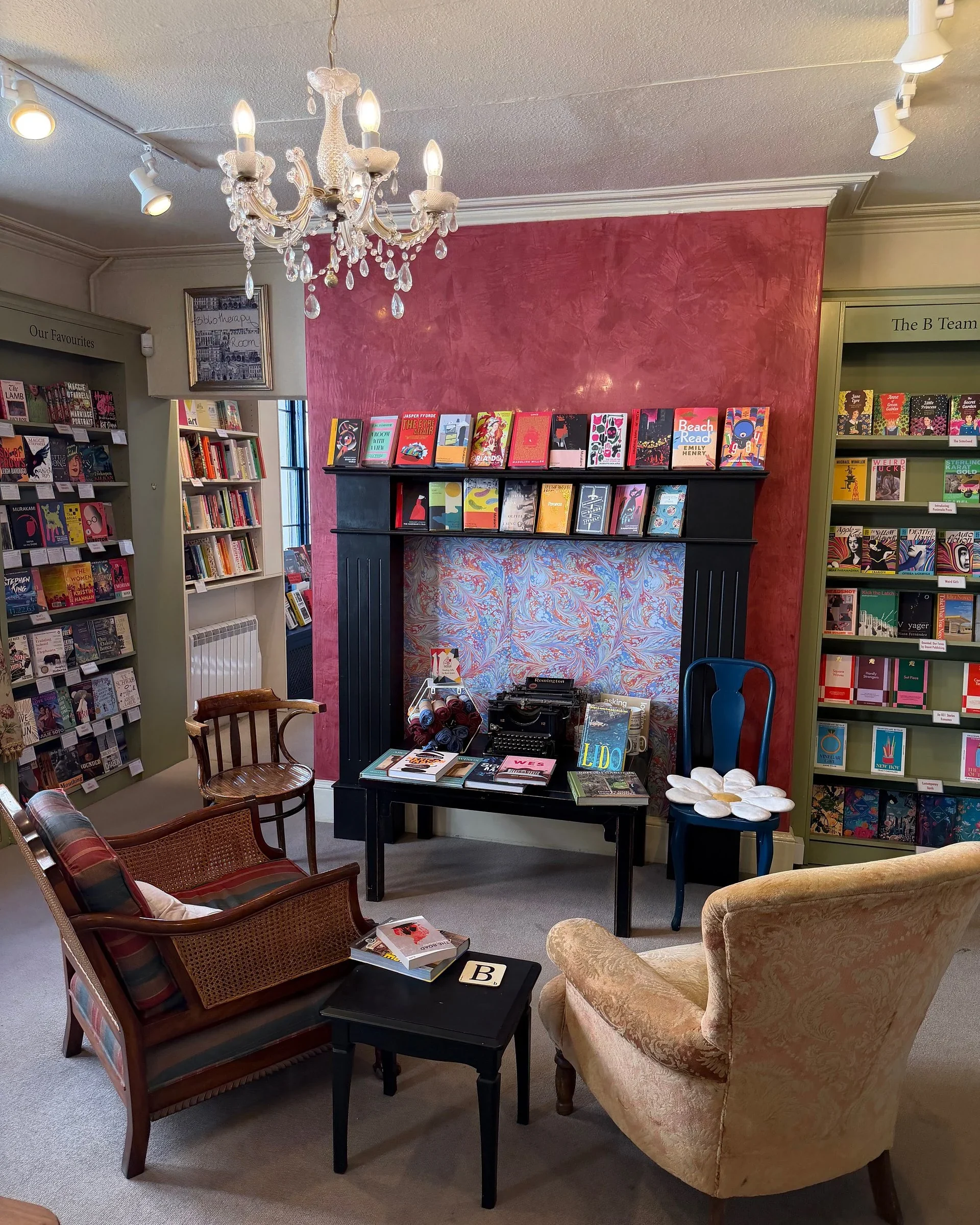 Cozy bookshop corner with armchairs, a crystal chandelier, a vintage typewriter, and shelves of books