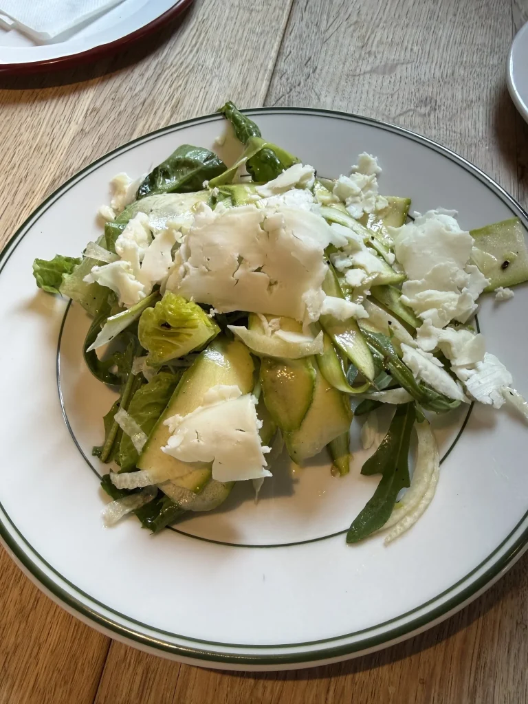 Shaved asparagus and greens salad topped with cheese on a white plate