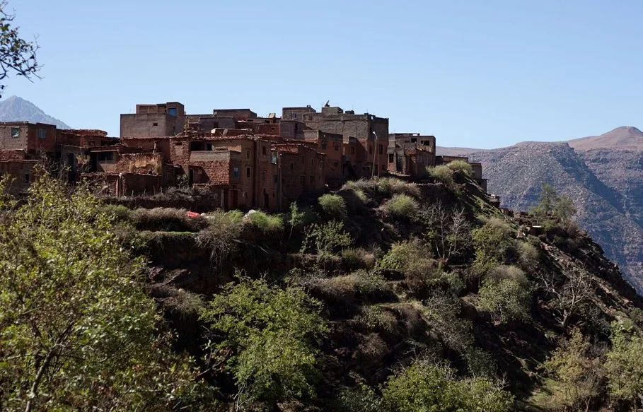 Red earth village on a green hillside with Atlas Mountain peaks behind