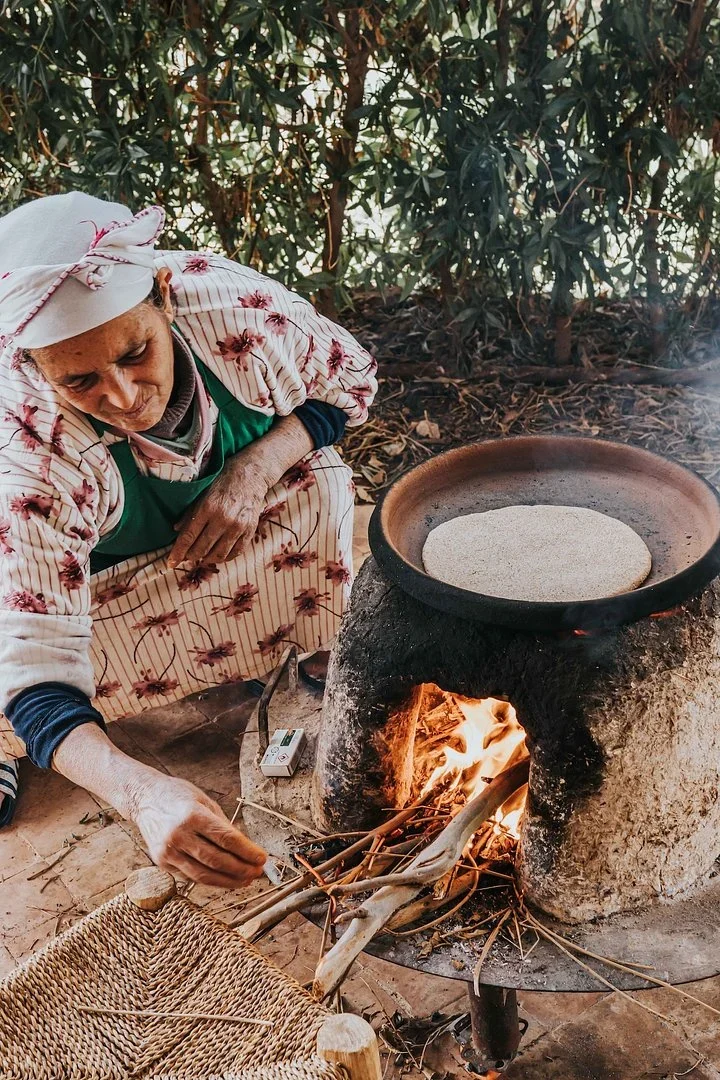 Moroccan woman baking round flatbread on a clay oven over a wood fire