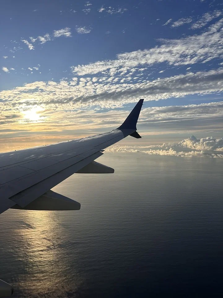 Airplane wing over the ocean at sunrise with scattered clouds