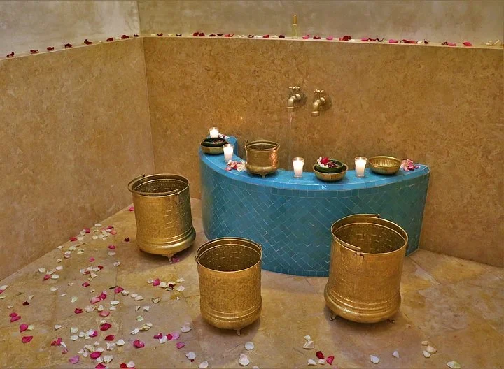 Hammam with brass buckets, candles, rose petals, and a blue tiled basin