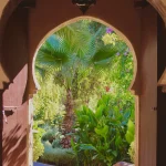 Moroccan keyhole archway with a lantern, opening onto a palm tree and garden path