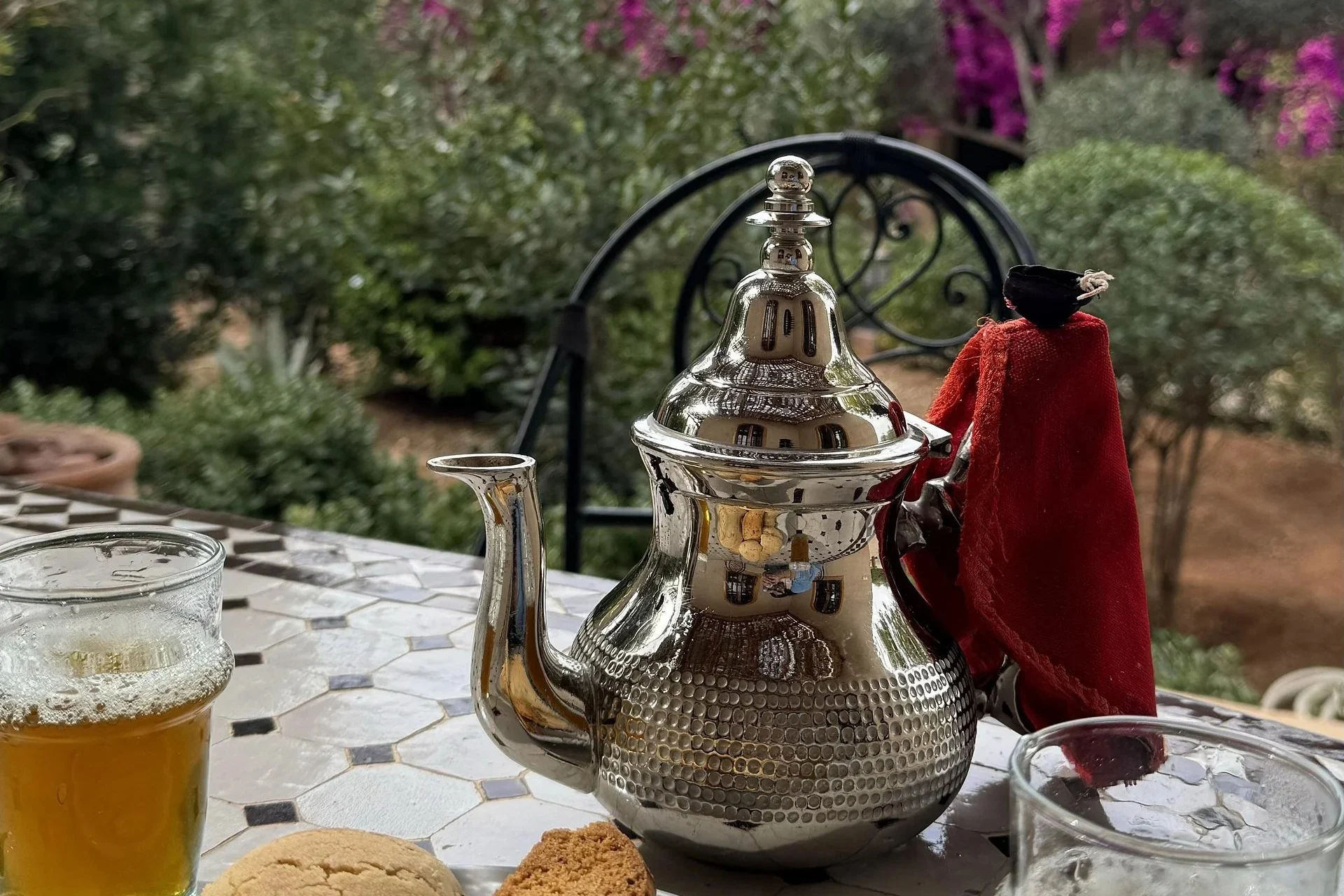 Silver Moroccan teapot and glasses of mint tea on a mosaic table in a garden with bougainvillea