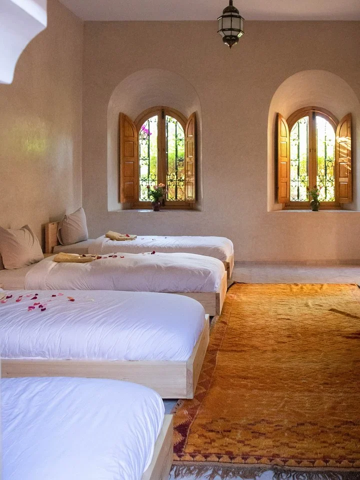 Bright room with several single beds, arched windows, and a woven rug