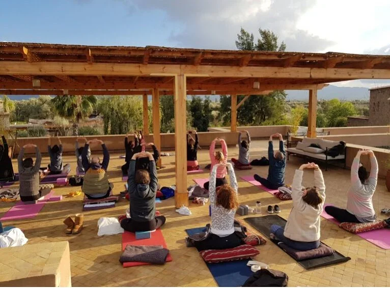 Guests stretching on mats under a wooden pergola on the rooftop, with trees and mountains beyond