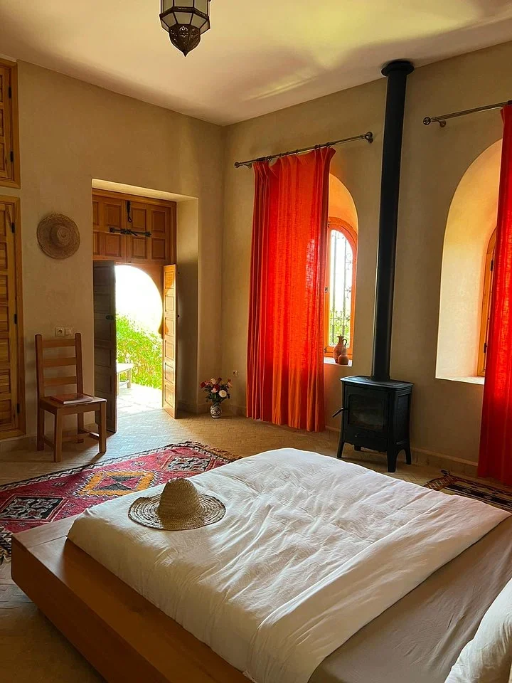 Bedroom with a double bed, orange curtains, a wood stove, and a door open to the garden