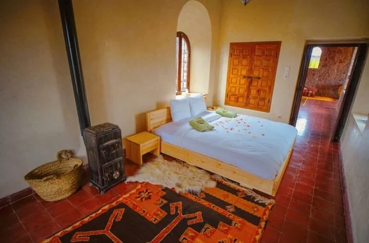 Bedroom with a double bed, a wood stove, a red tile floor, and a patterned rug