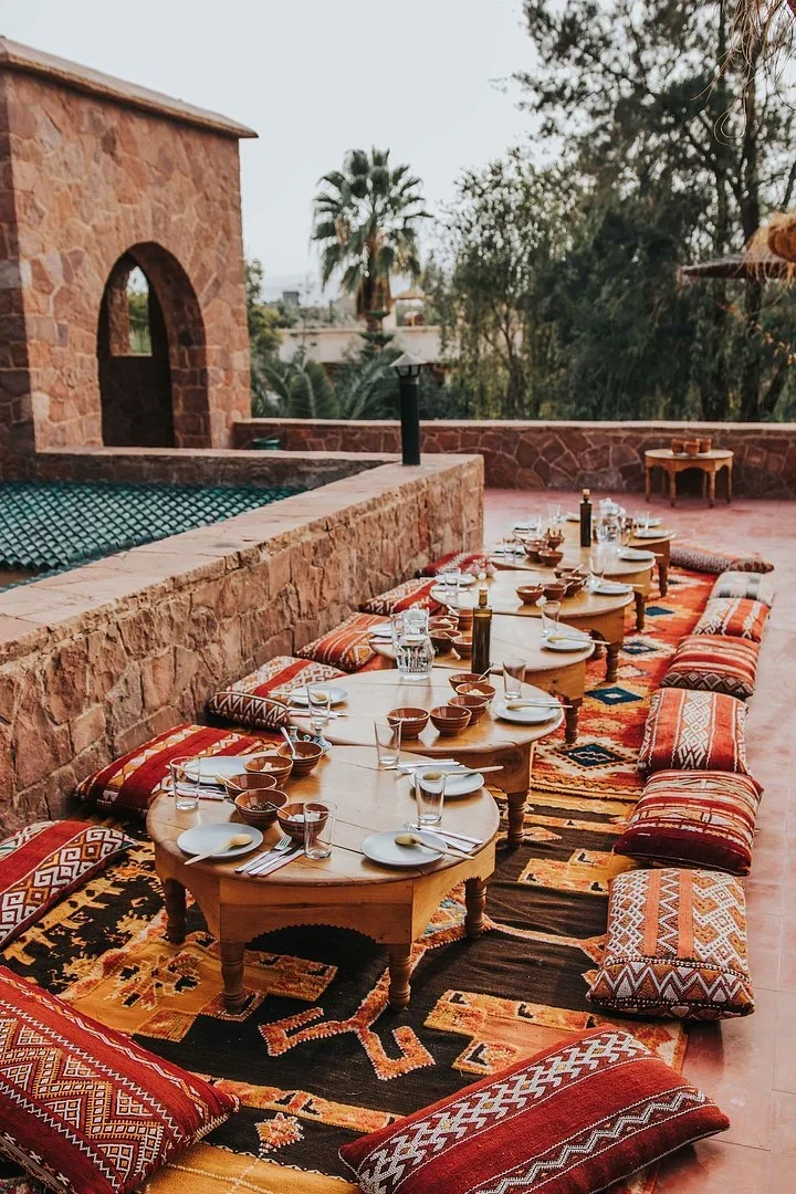 Low round tables set for a meal on a terrace, with Berber rugs and floor cushions