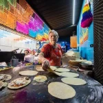 Cook pressing memelas on a hot comal at a market stall in Oaxaca