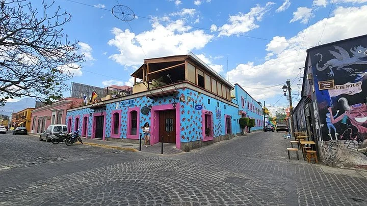 Bright blue building painted with red flowers on a cobblestone corner in Oaxaca, next to a wall mural