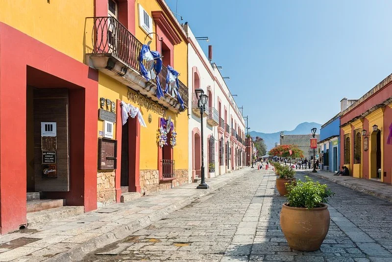 Colorful houses lining a cobblestone street in Oaxaca, with mountains at the far end