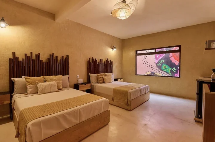 Hotel room with two double beds, bamboo headboards, tan walls, and a window onto a painted mural