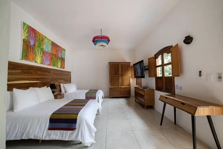 Spacious hotel room with two double beds, an agave painting, a wooden wardrobe, and a writing desk