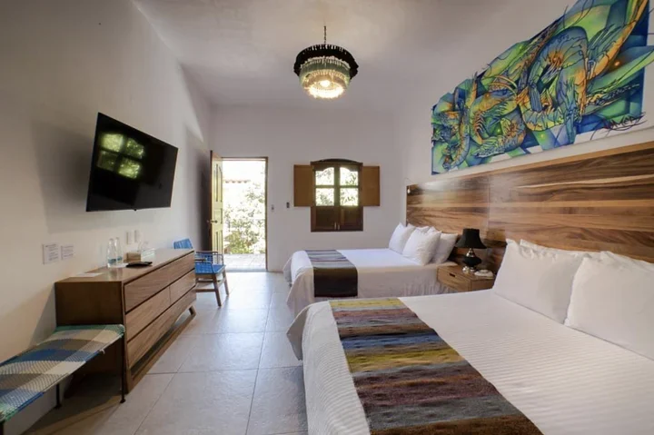 Hotel room with two double beds, woven runners, a wooden headboard, and a large colorful mural above
