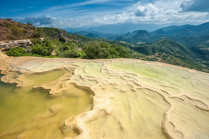 Terraced mineral pools at Hierve el Agua in Oaxaca overlooking green mountains under a blue sky