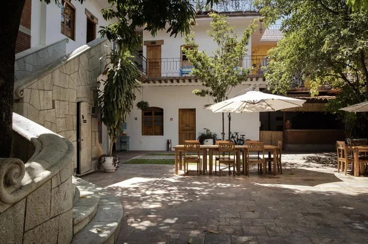 Sunny stone courtyard at a boutique hotel in Oaxaca with a long wooden table, an umbrella, and trees