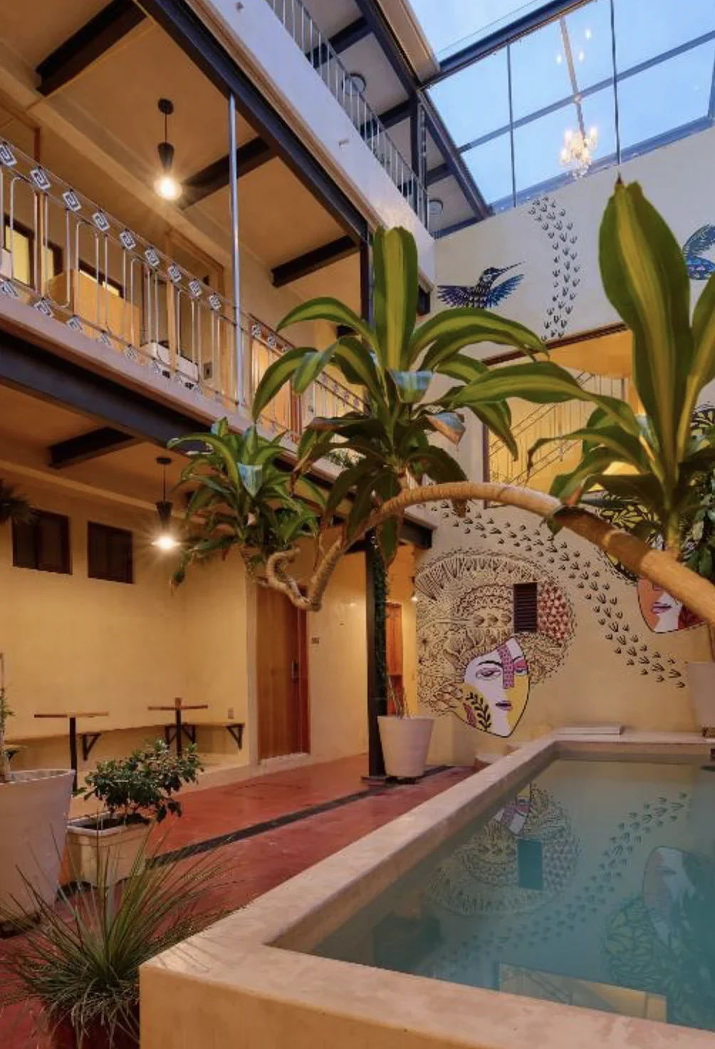 Courtyard plunge pool at a boutique hotel in Oaxaca, with painted murals of faces and hummingbirds, potted plants, and balconies above