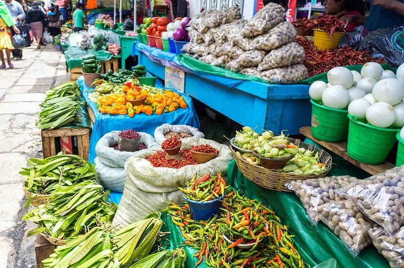 Market stall with baskets of dried chiles, fresh peppers, onions, peanuts, and green beans on a cobblestone lane