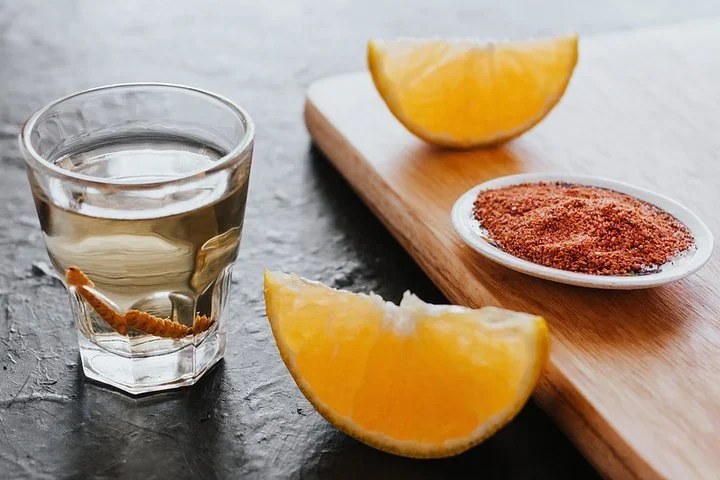 Glass of mezcal with orange slices and a dish of chile salt on a wooden board