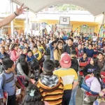Room full of smiling students at a community event in Oaxaca, with a man speaking into a microphone