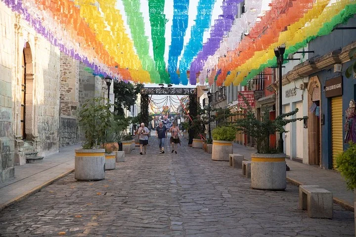 Colorful papel picado banners strung over a cobblestone street in Oaxaca, with people walking below