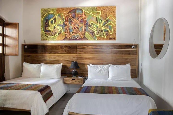 Hotel room with two double beds under a large painting, a wooden headboard, and a round mirror