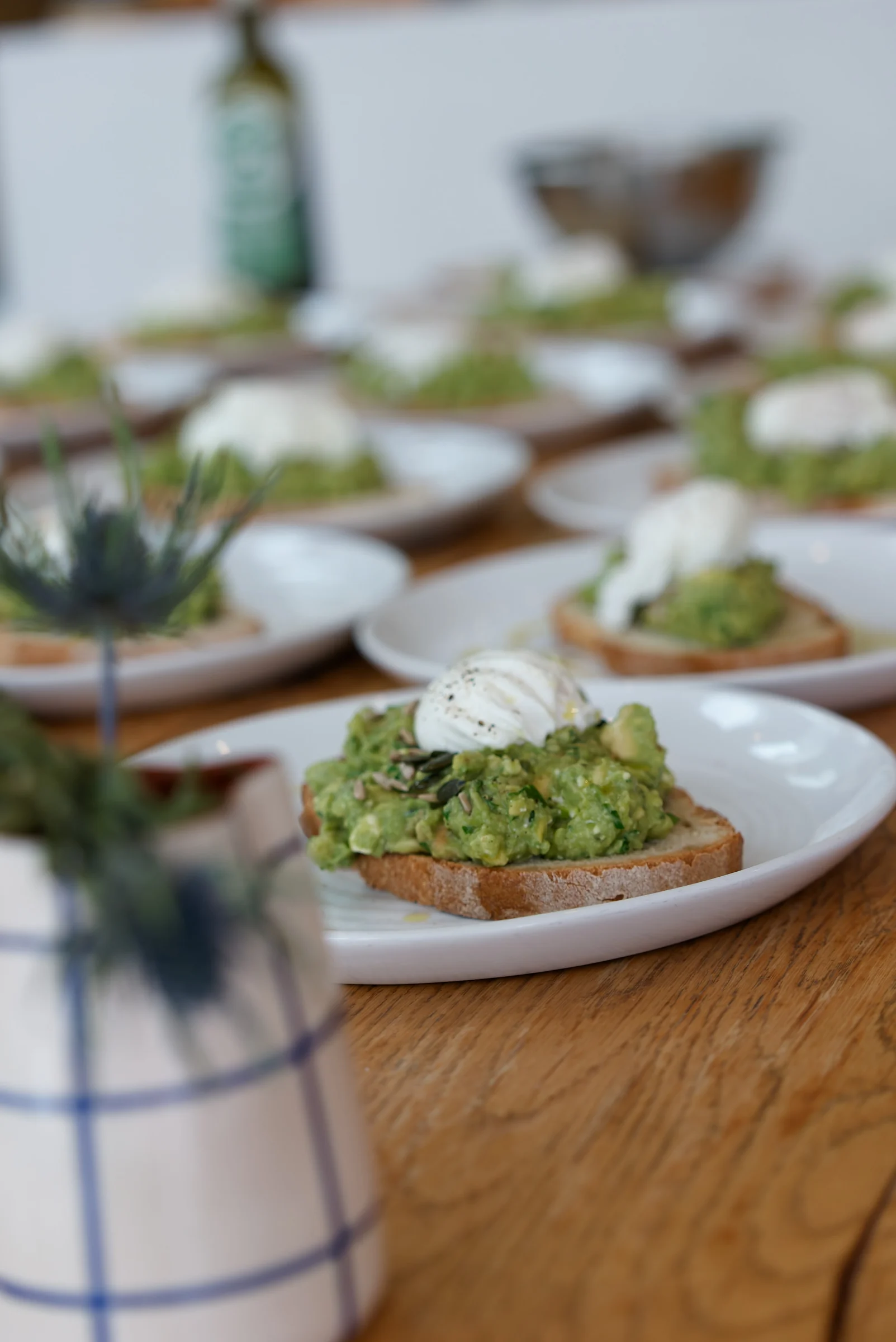 Plates of smashed avocado toast topped with poached eggs and seeds on a wooden table