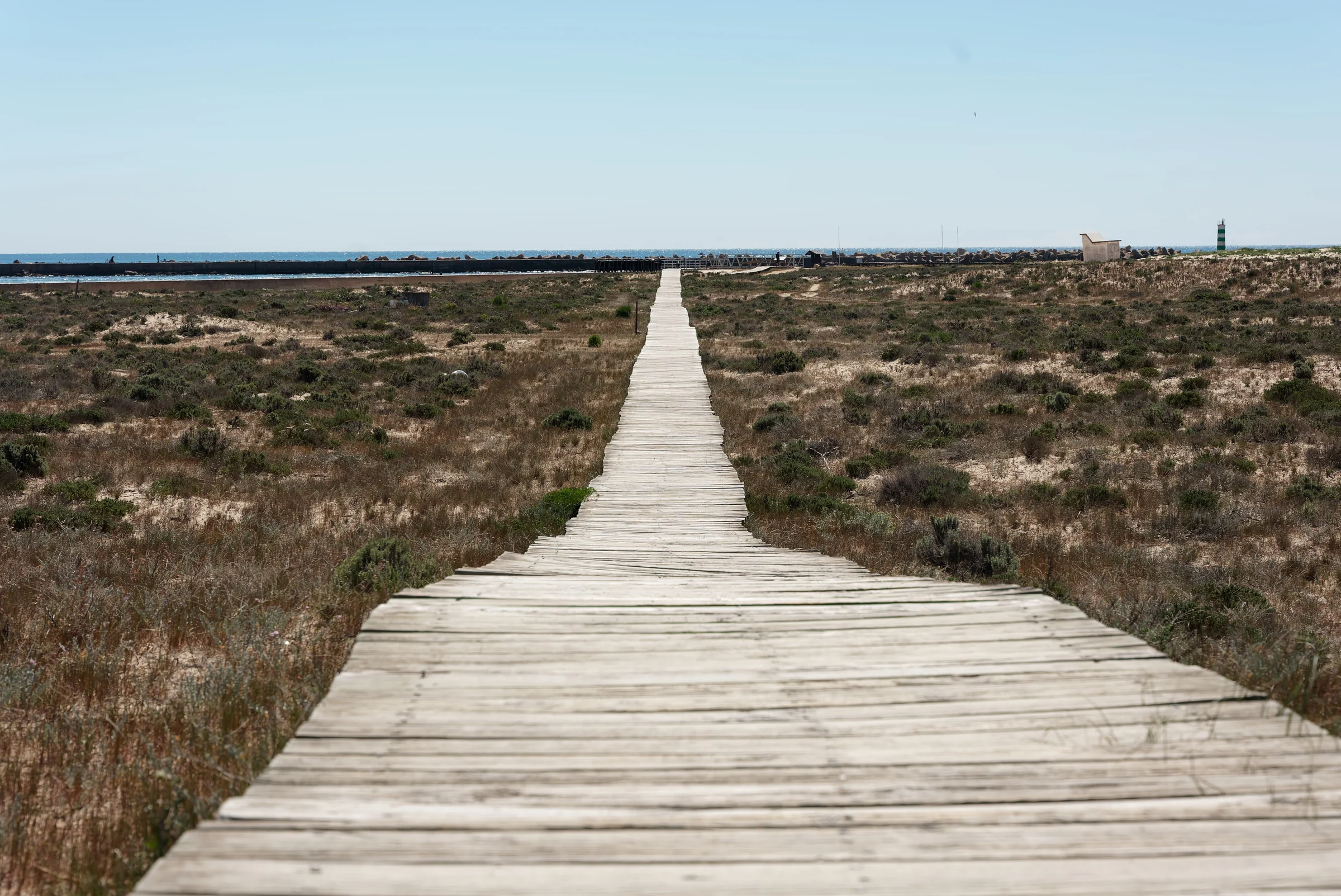 Weathered wooden boardwalk running through coastal dunes toward the sea in the Algarve