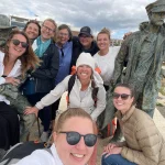 Laughing group of retreat guests posing with bronze statues on a waterfront promenade