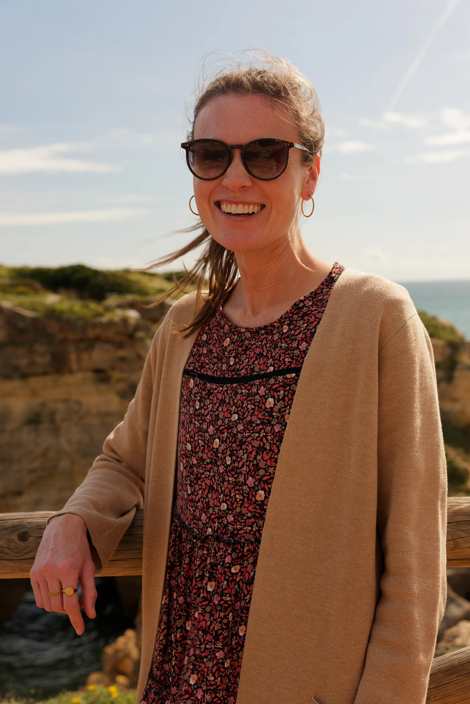 Smiling guest in sunglasses leaning on a railing above golden sea cliffs