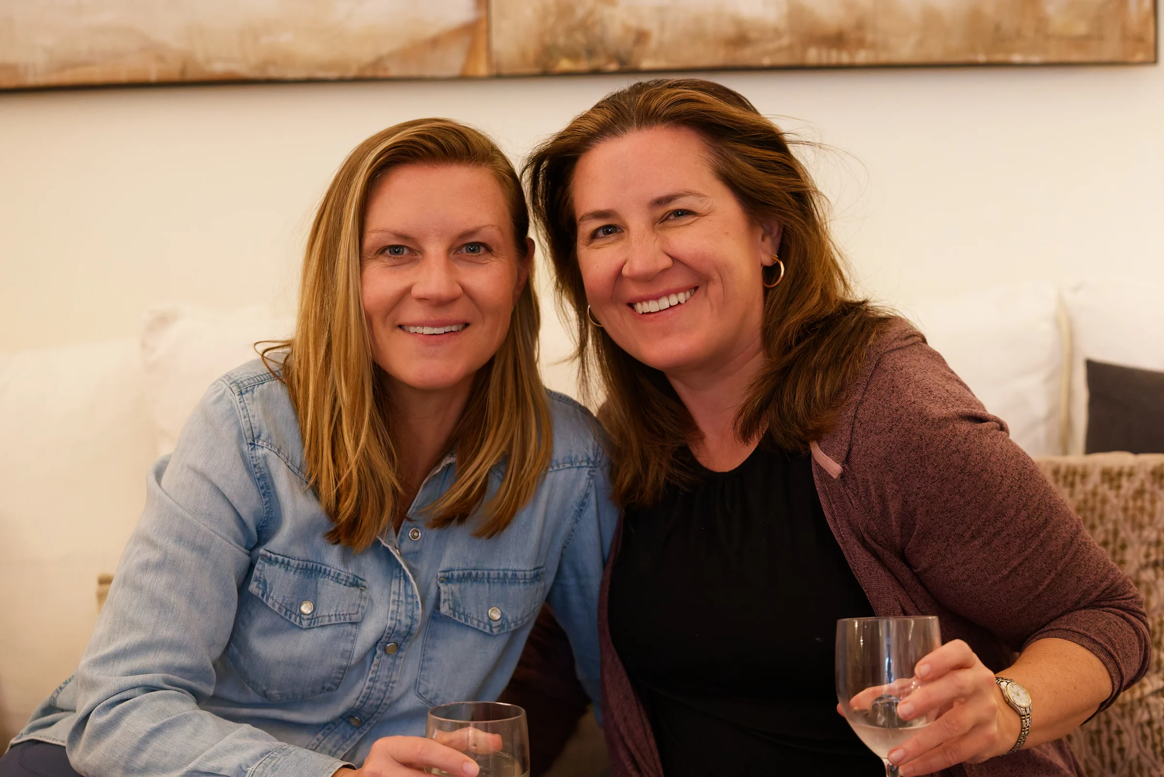 Two smiling guests raising wine glasses on a sofa