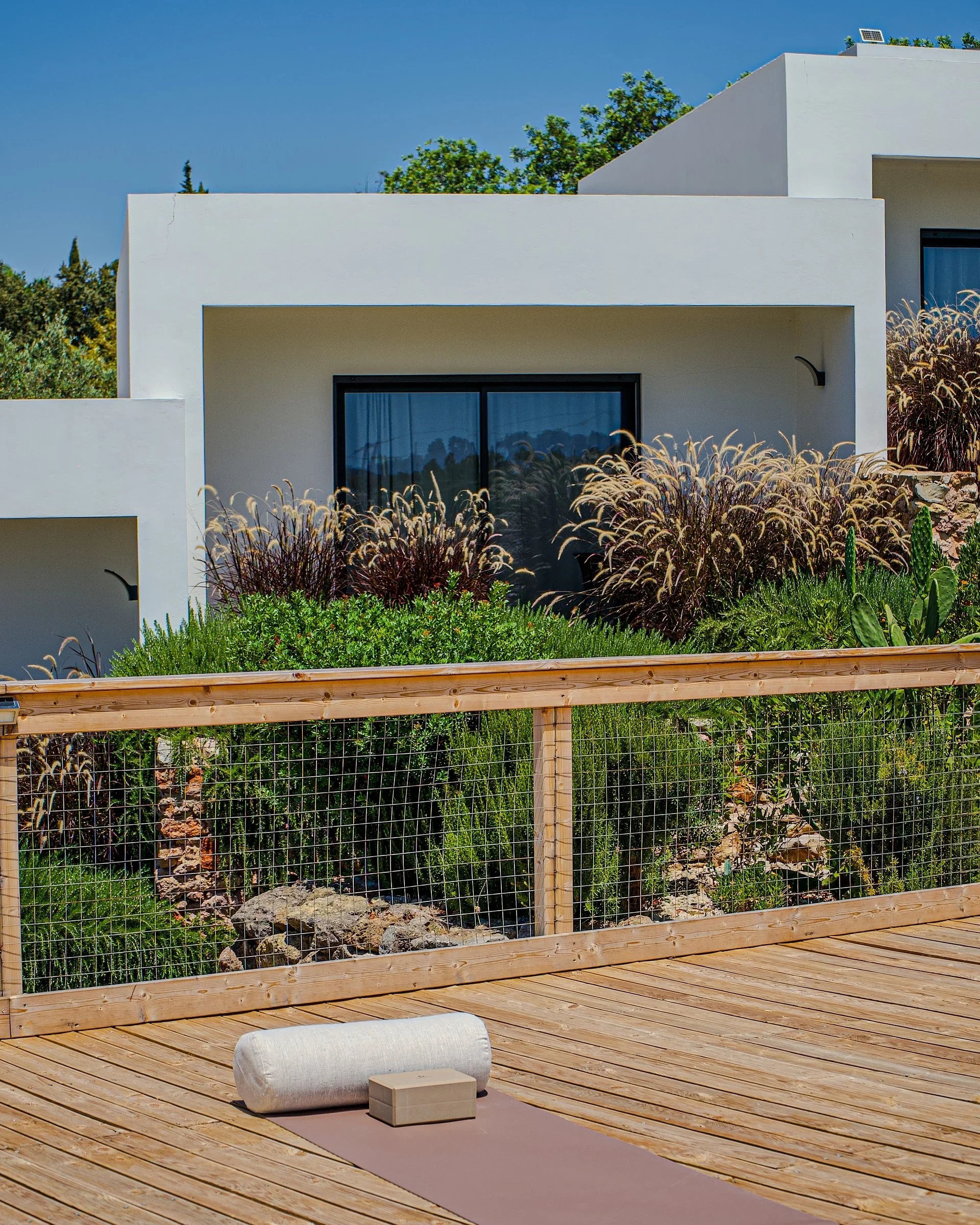 Mat, bolster, and block on a wooden deck in front of white villas and ornamental grasses