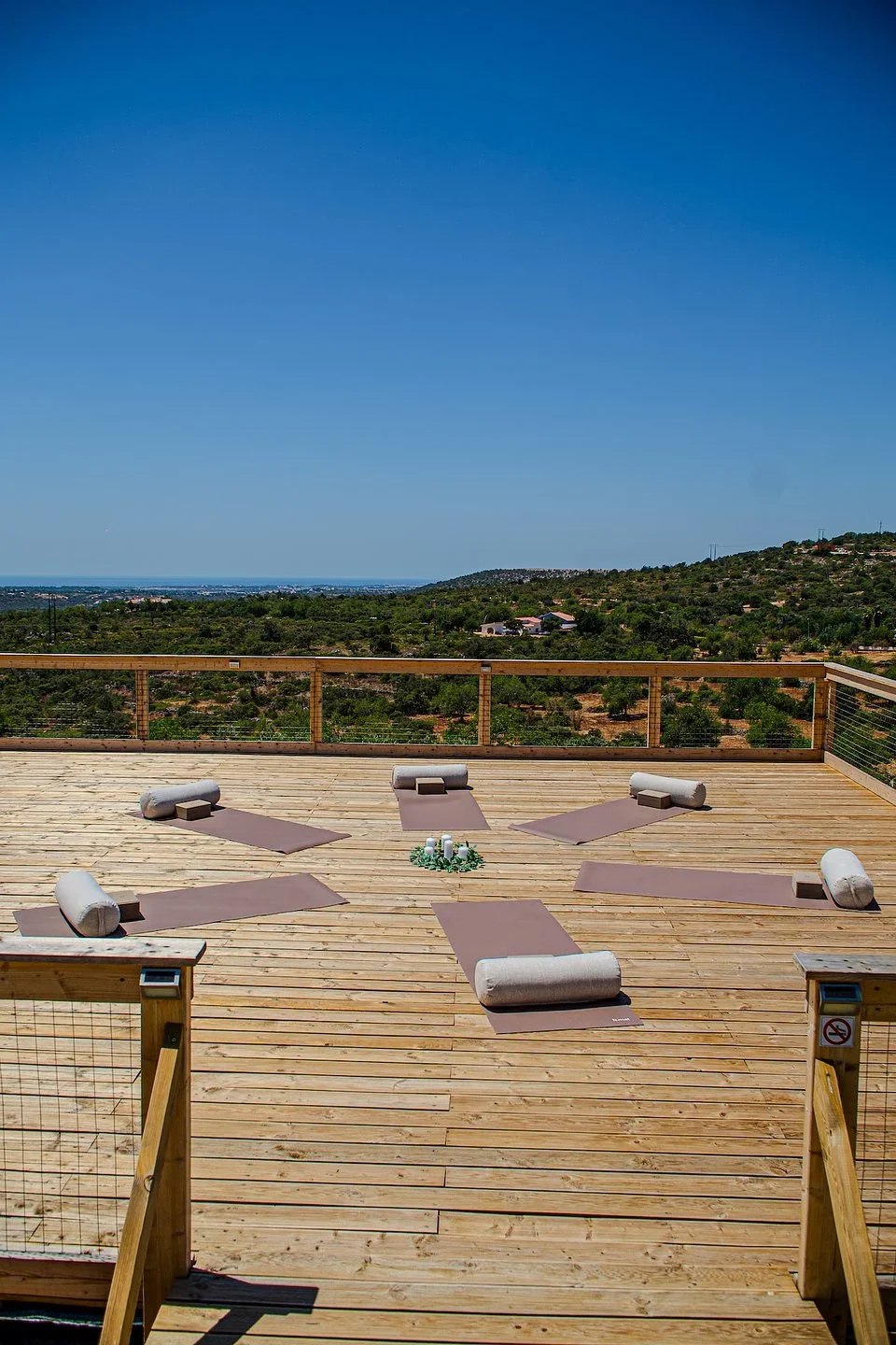 Mats and bolsters arranged in a circle on a wooden deck with views over green hills toward the sea