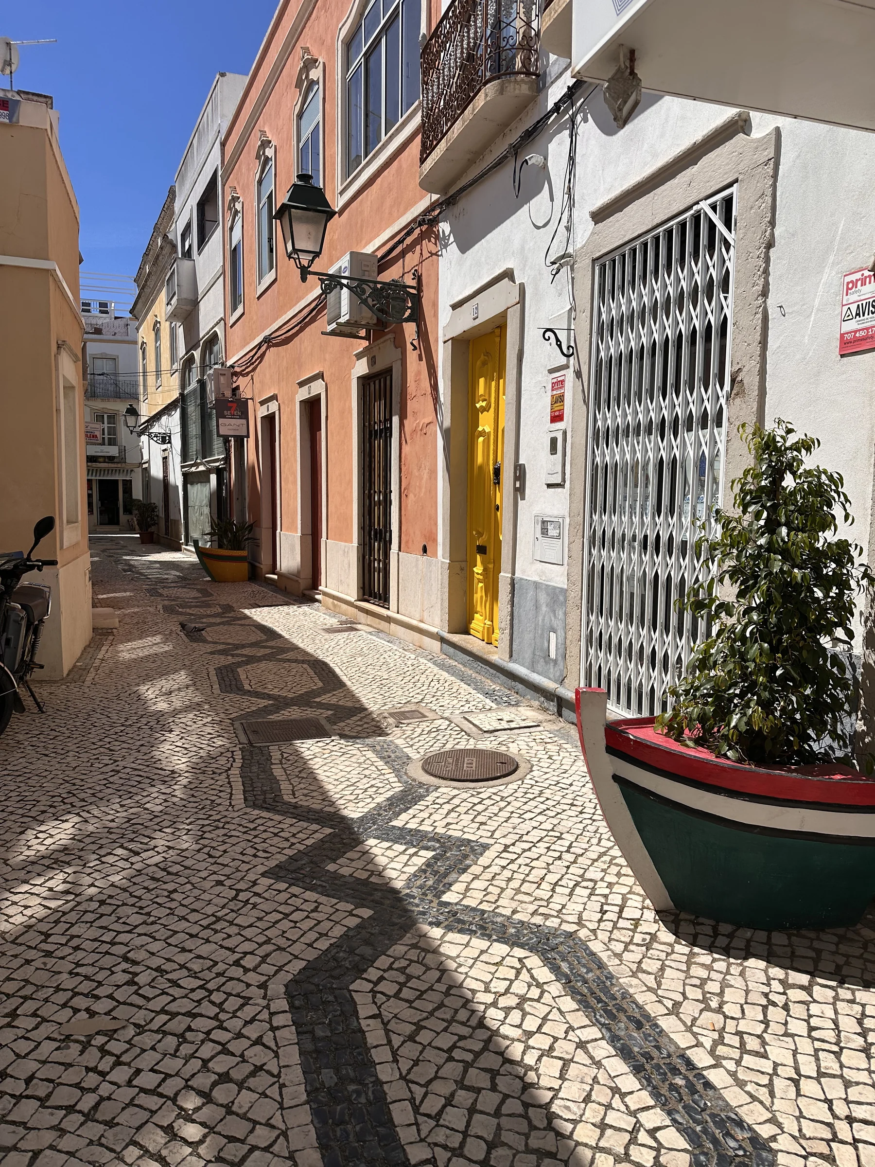 Pedestrian street with wave-patterned cobblestones, pastel buildings, and potted plants