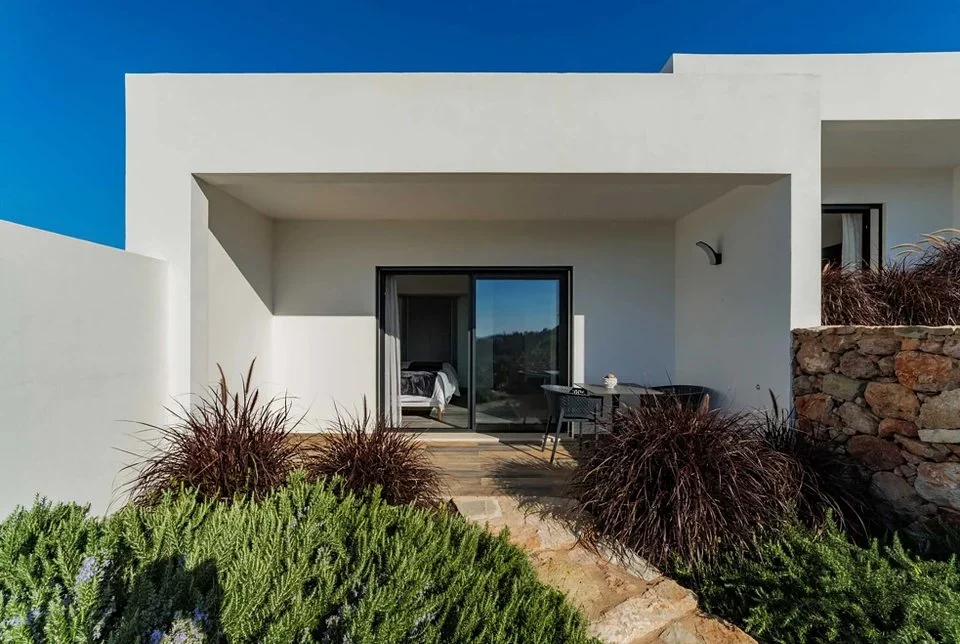 White guest room with sliding glass doors opening onto a patio with a table and ornamental grasses