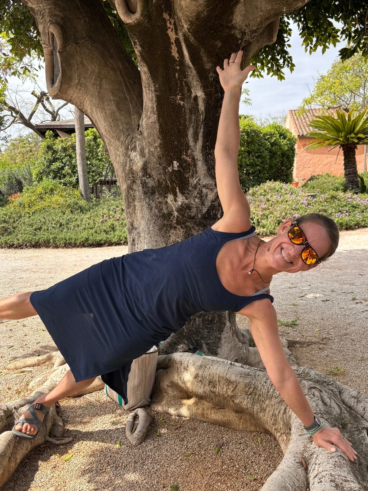 Smiling woman in sunglasses holding a side plank on the roots of a huge tree