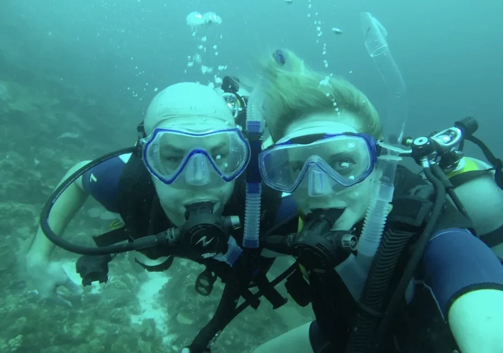 Lindsay and Ryan are taking an underwater selfie in scuba masks above a reef